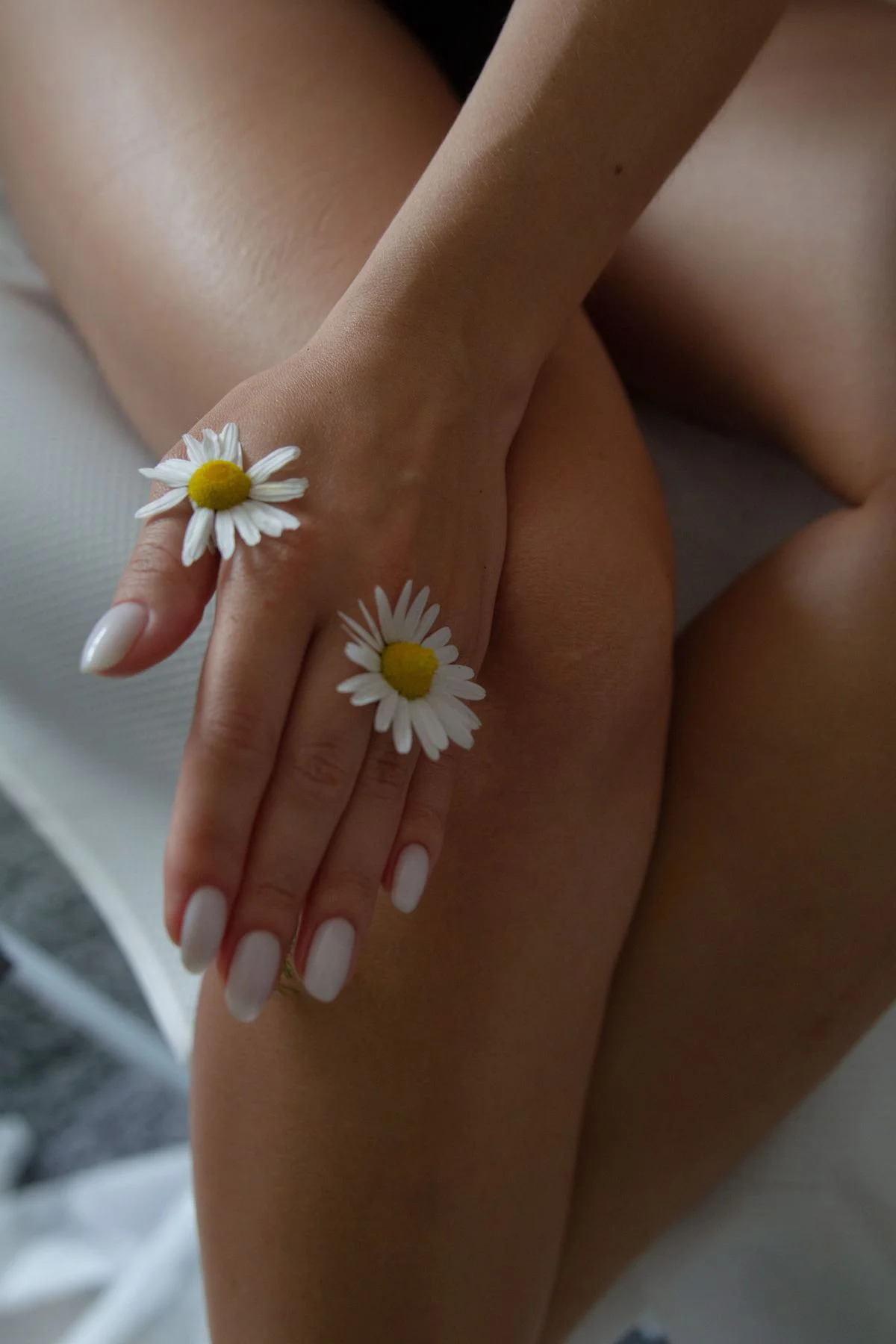 Main posée sur une jambe, une marguerite entre les doigts